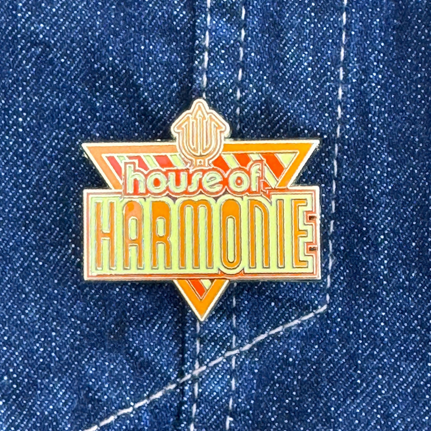 House of Harmonie logo pin in yellow and orange from one of the best drag shows ever.