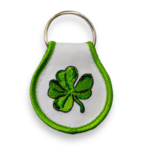 Double sided, droplet-shaped keychain embroidered with green border and four-leaf shamrock, by visual artist Jaik Olson.