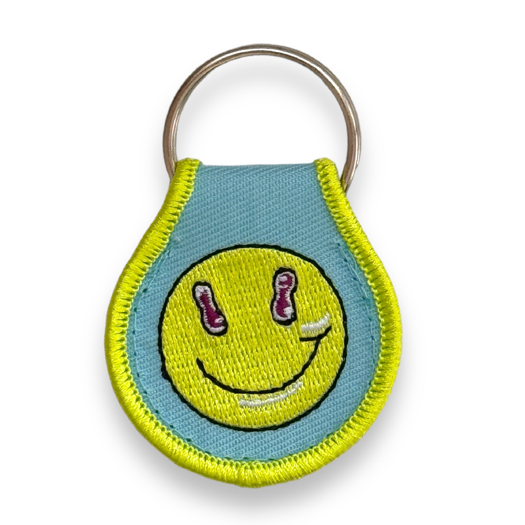 Unique key tag in light blue with lime-green border and iconic Puppyteeth smiley-face. Droplet-shaped, on ring.