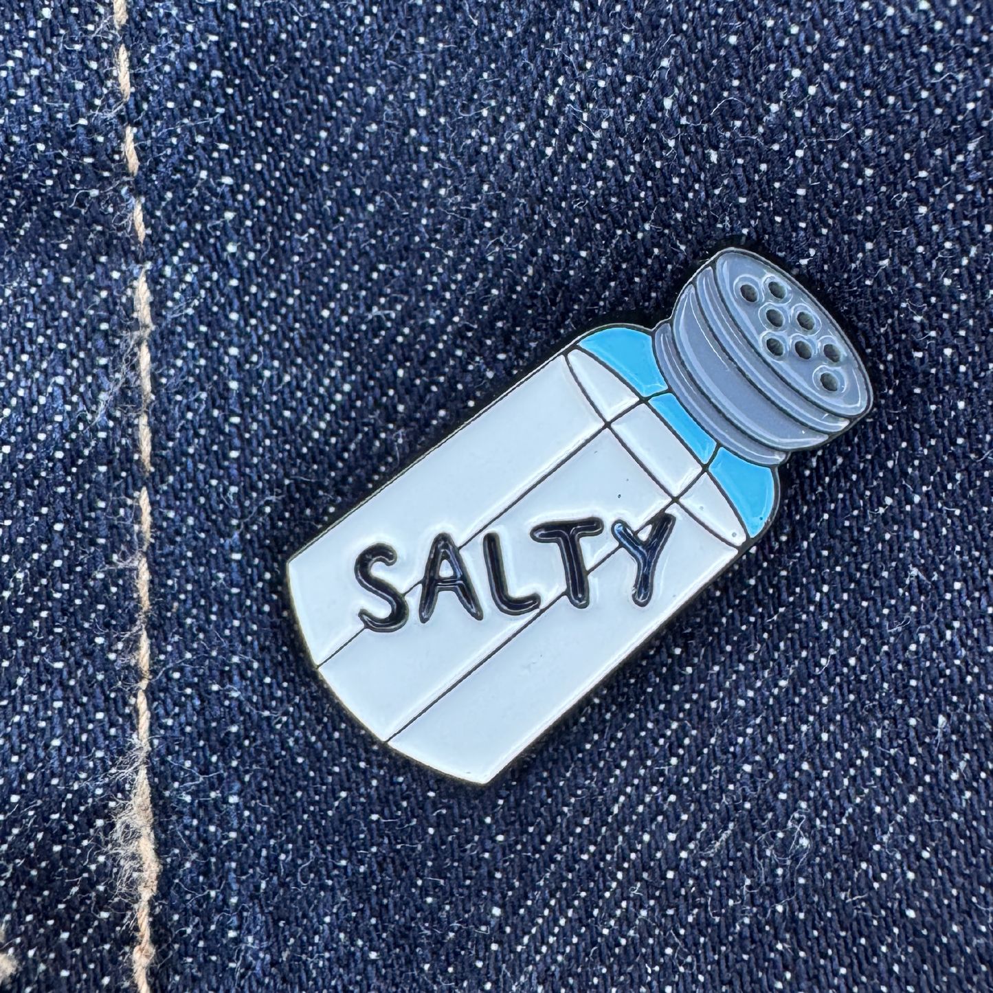 Salt shaker shaped lapel pin with the word Salty written on it.