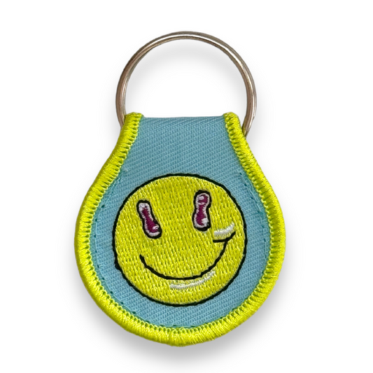 Blue droplet-shaped keychain embroidered with green border and green smiley-face.