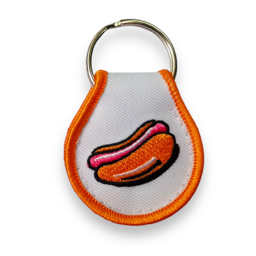 White droplet-shaped keychain embroidered with orange border and an orange and red hotdog.